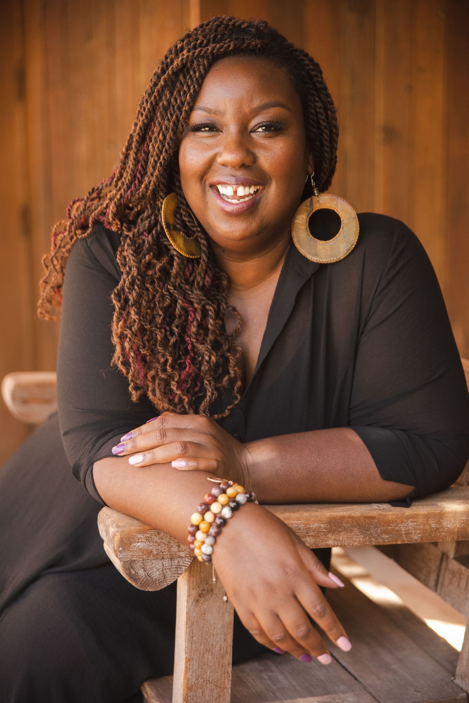 Kali Shelton seated, leaning in and smiling, with braids
